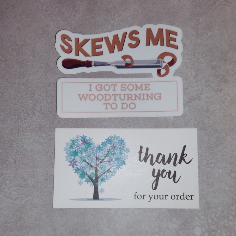 May include: Two stickers with woodturning themed text. The top sticker is brown and says "Skews Me" with a woodturning chisel. The bottom sticker is white and says "I got some woodturning to do". A white card with a blue snowflake tree and the text "thank you for your order" is also shown.