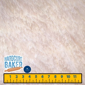 May include: A close-up of a white marble surface with a subtle veined pattern. A ruler with black markings is placed at the bottom of the image. A sticker with the text "HARDCORE BAKER" and a rolling pin is placed on the left side of the image. A small blue sticker with a dolphin logo is placed above the ruler.