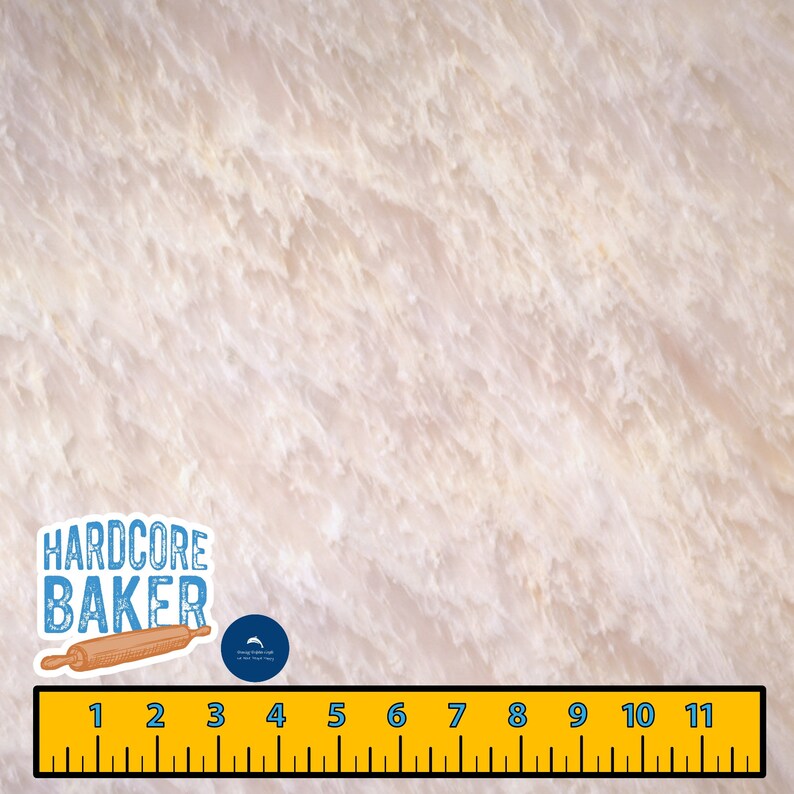 May include: A close-up of a white marble surface with a subtle veined pattern. A ruler with black markings is placed at the bottom of the image. A sticker with the text "HARDCORE BAKER" and a rolling pin is placed on the left side of the image. A small blue sticker with a dolphin logo is placed above the ruler.