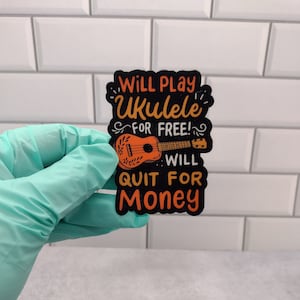 May include: Black and orange sticker with a ukulele and the text "Will Play Ukulele for Free! Will Quit for Money."