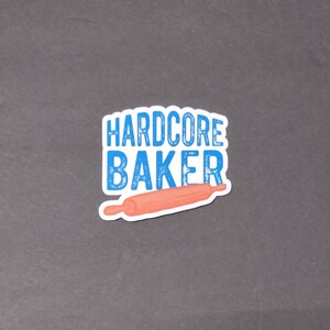 May include: A blue and white sticker with the text "HARDCORE BAKER" and a pink rolling pin.