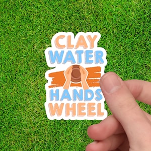 May include: A white sticker with blue and orange text that reads "Clay Water Hands Wheel". The sticker has a graphic of hands forming a clay pot.