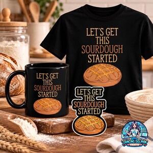 May include: A black t-shirt, a black ceramic mug, and a sticker, each featuring a graphic of a round loaf of bread and the text LET'S GET THIS SOURDOUGH STARTED in orange lettering. The items are arranged together on a wooden surface.