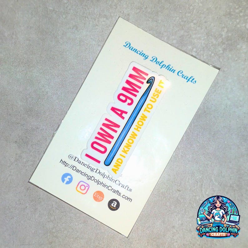 K&ouml;nnte beinhalten: Ein gelber und rosa Aufkleber mit einem blauen H&auml;kelhaken und dem Text "I own a 9mm and I know how to use it". Der Aufkleber befindet sich auf einem wei&szlig;en Hintergrund mit dem Text "Dancing Dolphin Crafts" und Social-Media-Symbolen.