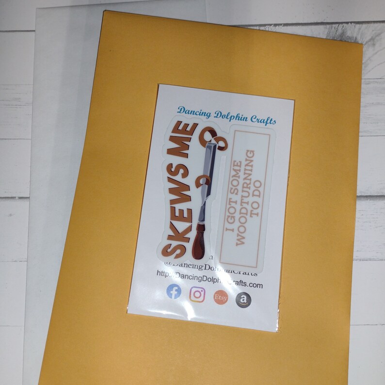 May include: A white sticker with a brown woodturning chisel and the text "SKEWS ME" and "I GOT SOME WOODTURNING TO DO". The sticker is on a yellow envelope.