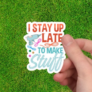 May include: A white sticker with the text "I stay up late to make stuff" in colorful lettering. The sticker features a hot glue gun, yarn, and beads.