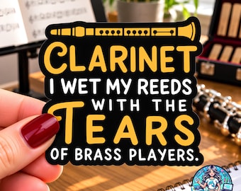 May include: A black die-cut sticker featuring a yellow graphic of a clarinet at the top and the white and yellow text: CLARINET I WET MY REEDS WITH THE TEARS OF BRASS PLAYERS. The sticker has a smooth finish and a distinct, bold, and legible font.