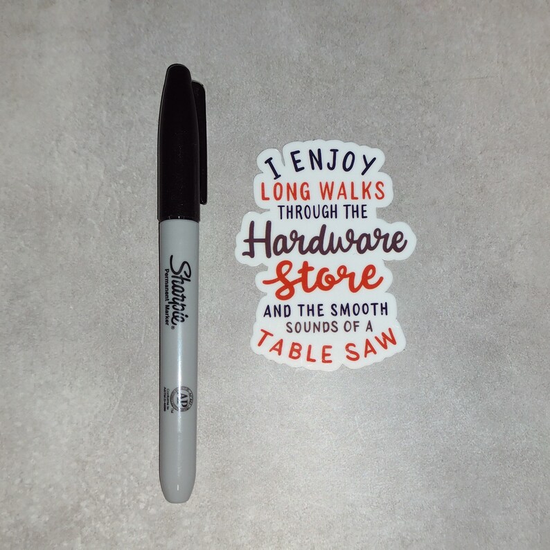 May include: A white sticker with the text "I enjoy long walks through the hardware store and the smooth sounds of a table saw" in black and red lettering.