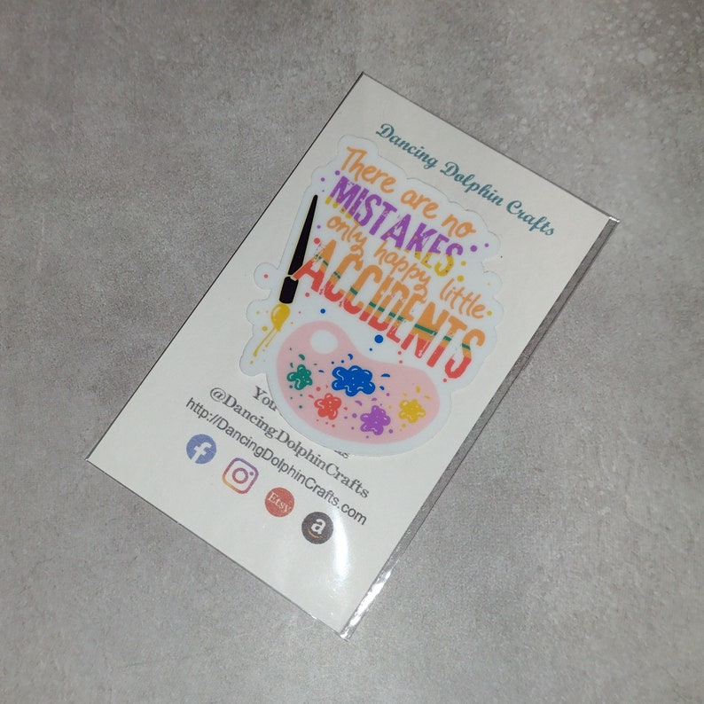 Puede incluir: Una pegatina con una paleta de pintura rosa y un pincel con el texto "No hay errores, solo peque&ntilde;os accidentes felices." La pegatina est&aacute; en una tarjeta blanca con el texto "Dancing Dolphin Crafts" y iconos de redes sociales.