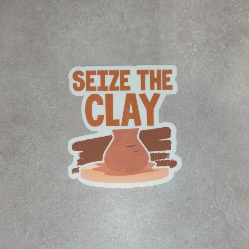K&ouml;nnte beinhalten: Ein wei&szlig;er Aufkleber mit braunen und orangen Akzenten. Der Aufkleber zeigt eine Tonvase auf einer T&ouml;pferscheibe und den Text "Seize the Clay".