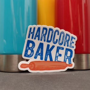 May include: White sticker with blue text that reads "HARDCORE BAKER" and a red and orange illustration of a rolling pin.