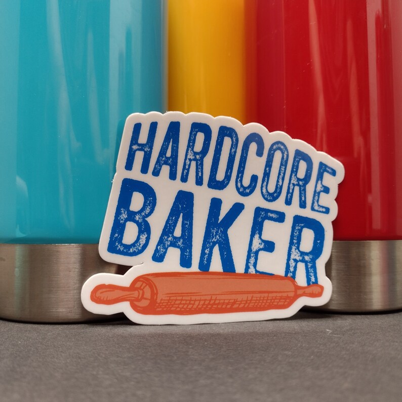 May include: White sticker with blue text that reads "HARDCORE BAKER" and a red and orange illustration of a rolling pin.