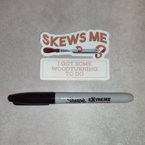 May include: A sticker with the text "Skews Me" and a woodturning tool. Below the sticker is a white rectangle with the text "I got some woodturning to do". A black Sharpie Extreme fade resistant marker is in the foreground.