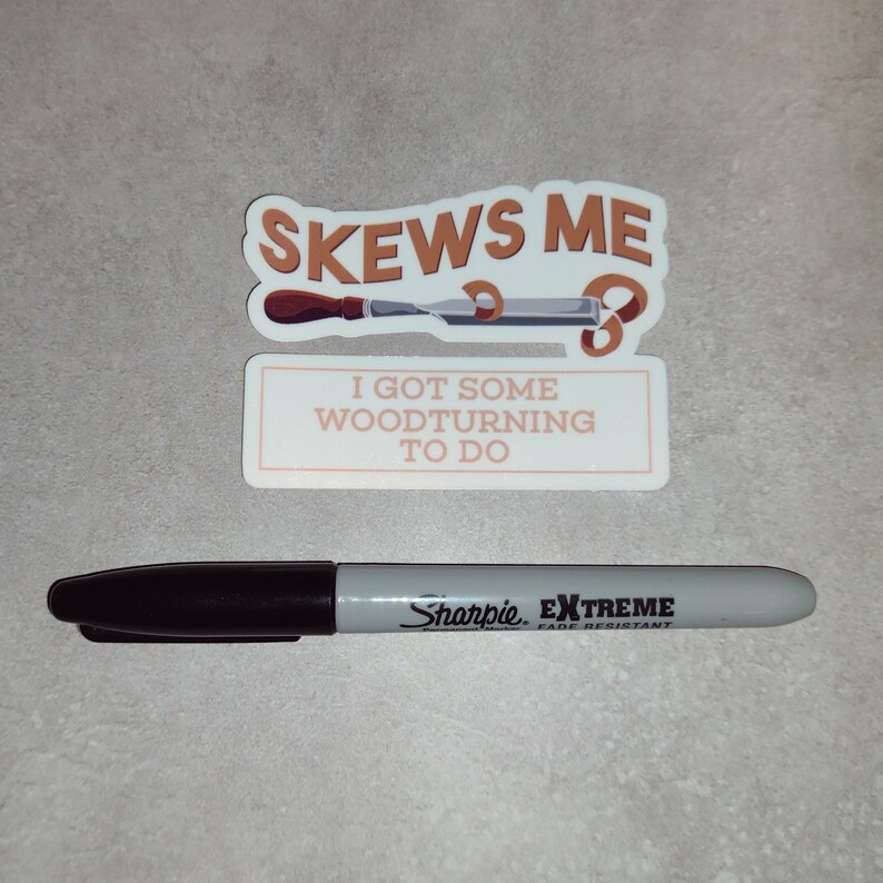 May include: A sticker with the text "Skews Me" and a woodturning tool. Below the sticker is a white rectangle with the text "I got some woodturning to do". A black Sharpie Extreme fade resistant marker is in the foreground.
