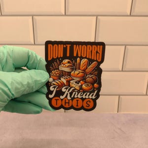 May include: A black and orange sticker with the text "Don't Worry I Knead This" and a cartoon illustration of various breads and pastries.