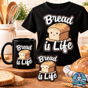May include: A black t-shirt, a black ceramic mug, and a sticker, each featuring a graphic of a smiling loaf of bread on a plate with the text Bread is Life in white lettering. The items are arranged together on a wooden surface.