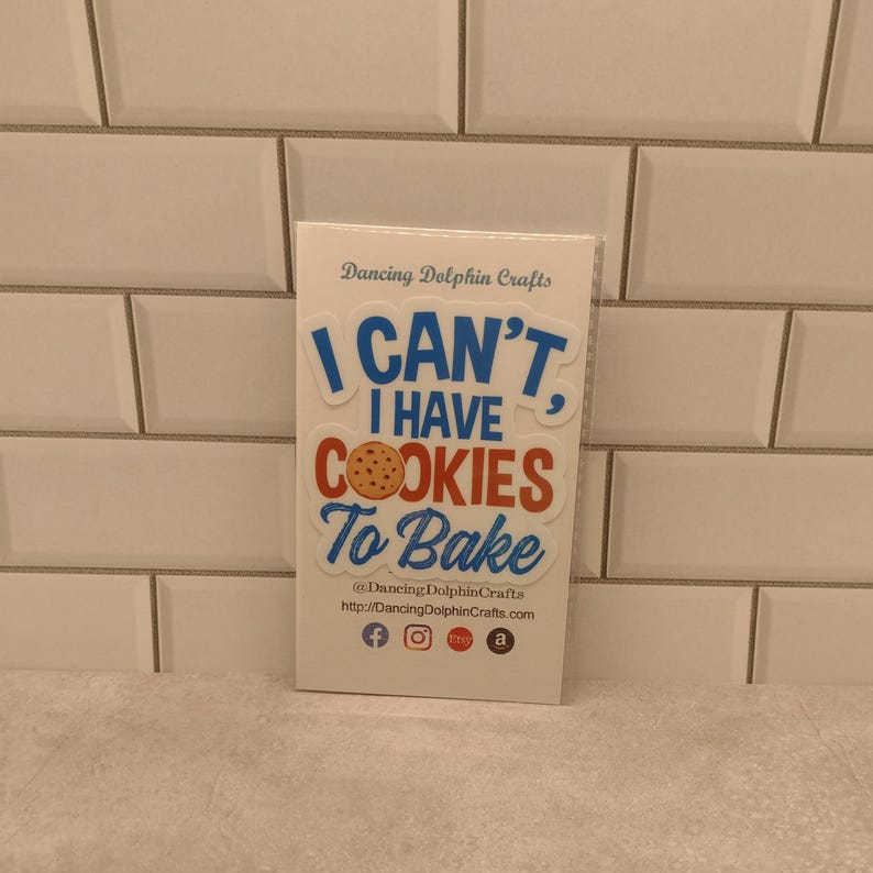 Może przedstawiać: Biała naklejka z niebieskim i czerwonym tekstem, kt&oacute;ry brzmi "I CAN'T, I HAVE COOKIES To Bake". Naklejka przedstawia brązowe ciasteczko z czekoladowymi kawałkami.