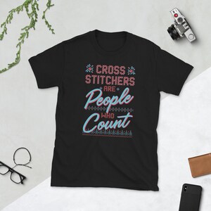May include: Black t-shirt with a white and pink design that says "Cross Stitchers are People Who Count".