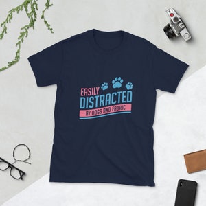 Könnte beinhalten: Marineblaues T-Shirt mit einem hellblauen und rosafarbenen Aufdruck, auf dem "Leicht abgelenkt von Hunden und Stoffen" steht.