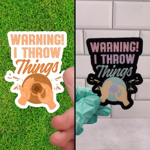 May include: Two vinyl stickers with the text "WARNING! I THROW THINGS" in a retro font. The stickers feature a hand throwing a clay pot on a pottery wheel. One sticker is on a green background and the other is on a white tiled background.