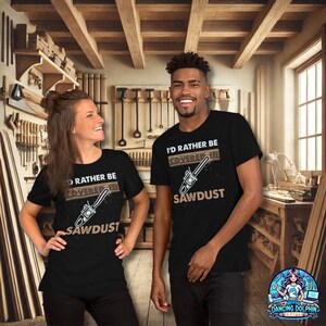 K&ouml;nnte beinhalten: Zwei Personen tragen schwarze T-Shirts mit einem wei&szlig;en Grafikdesign. Das Grafikdesign zeigt eine Kettens&auml;ge und den Text "I'd rather be covered in sawdust".