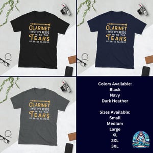 May include: A collection of three short-sleeve t-shirts in black, navy, and dark heather gray. Each shirt features a graphic of a clarinet and the text: CLARINET I WET MY REEDS WITH THE TEARS OF BRASS PLAYERS in white and yellow.