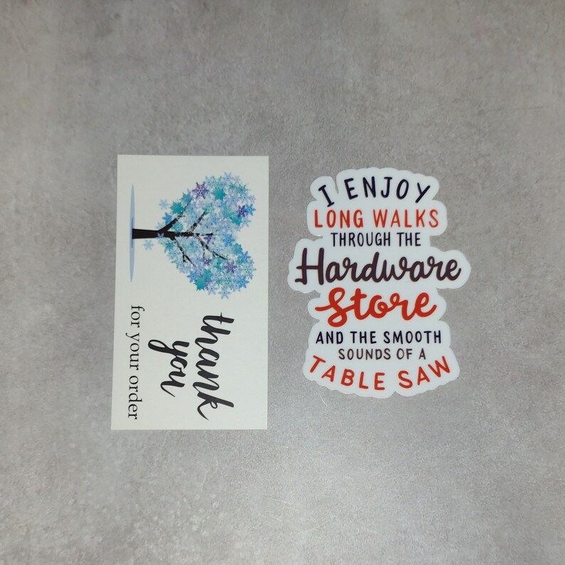 May include: A thank you card with a blue snowflake tree design and the text "thank you" and "for your order". A sticker with the text "I enjoy long walks through the hardware store and the smooth sounds of a table saw".