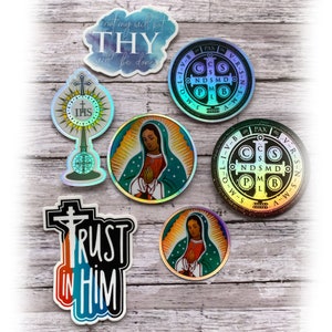 May include: A collection of seven religious stickers featuring two circular Saint Benedict medals with holographic finishes, two circular Our Lady of Guadalupe stickers, a monstrance sticker, and two die-cut stickers with the text Not my will but THY will be done and TRUST IN HIM.