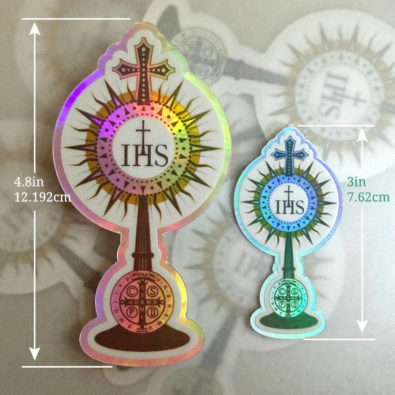May include: Two holographic stickers depicting a monstrance with a cross and the letters IHS. The larger sticker measures 12.192 cm in height, while the smaller sticker measures 7.62 cm in height. Both feature a circular base with text.