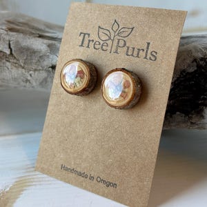 May include: A pair of round stud earrings made from natural wood slices with bark edges, featuring a glossy resin finish over a floral print. The earrings are attached to a brown card printed with the text Tree Purls and Handmade in Oregon.