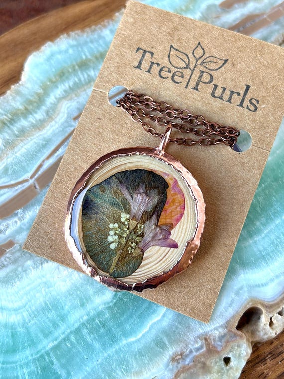 Real botanical specimens electroformed in copper — actual flowers fused into wearable metal art, not just resin casting.
