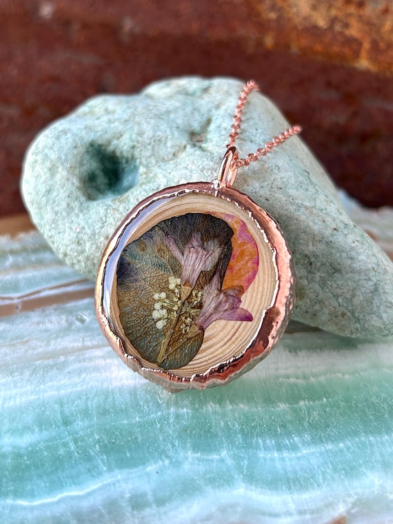 Real botanical specimens electroformed in copper — actual flowers fused into wearable metal art, not just resin casting.