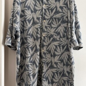 May include: A button-down shirt with a gray and white leaf pattern. The short-sleeved shirt has a collared neckline, a chest pocket, and a button-up front. The shirt is made of a soft, lightweight fabric.