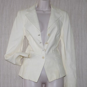 May include: Cream-colored blazer with a notched lapel, three-button closure, and two front pockets. The jacket has long sleeves and a tailored fit. The blazer is displayed on a mannequin.
