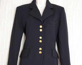 Puede incluir: Una blazer azul marino con botones dorados. La blazer tiene un diseño clásico con cuello con muescas, mangas largas y dos bolsillos delanteros. La blazer se muestra en un maniquí blanco.