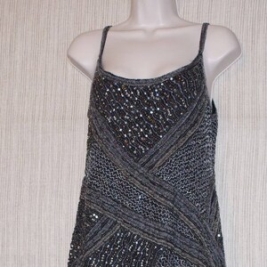 May include: A dark grey, sleeveless dress with a beaded bodice and skirt. The dress features a crisscross design on the bodice and a flowing skirt. The dress is displayed on a white mannequin.
