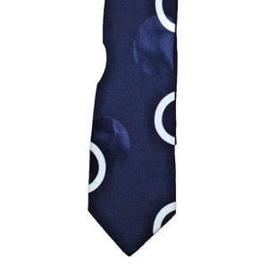Puede incluir: Corbata azul marino con un patrón repetido de semicírculos blancos y círculos azul oscuro. La corbata es un accesorio clásico, adecuado para vestimenta formal o de negocios. La corbata está hecha de un material liso, probablemente seda.