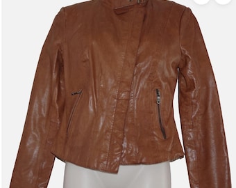 May include: A brown leather jacket with a stand-up collar and an asymmetrical zipper closure. The jacket features a small zippered pocket on the chest and a buckle detail at the collar. The jacket is displayed on a mannequin.