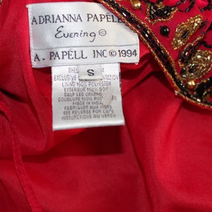 May include: Red evening dress with black and gold beaded embellishments. The label reads "ADRIANNA PAPELL Evening" and "A. PAPELL INC &copy; 1994". The dress is size S and made in India.