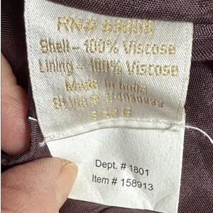 May include: A close-up of a white fabric label with gold text. The label states "Shell - 100% Viscose, Lining - 100% Viscose, Made in India." Additional text includes "Dept. # 1801" and "Item # 158913". The label is attached to a dark brown fabric.