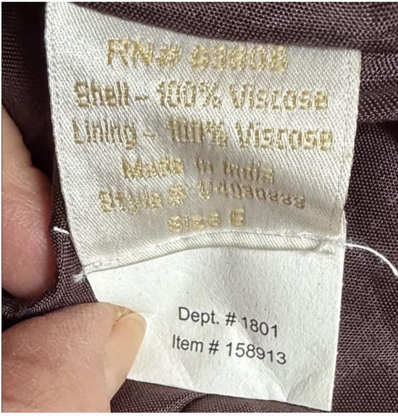 May include: A close-up of a white fabric label with gold text. The label states "Shell - 100% Viscose, Lining - 100% Viscose, Made in India." Additional text includes "Dept. # 1801" and "Item # 158913". The label is attached to a dark brown fabric.
