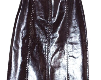 May include: A brown, knee-length skirt made of shiny, faux leather material. The skirt has vertical seams with small, silver-colored studs. It hangs from a metal hanger against a white background.
