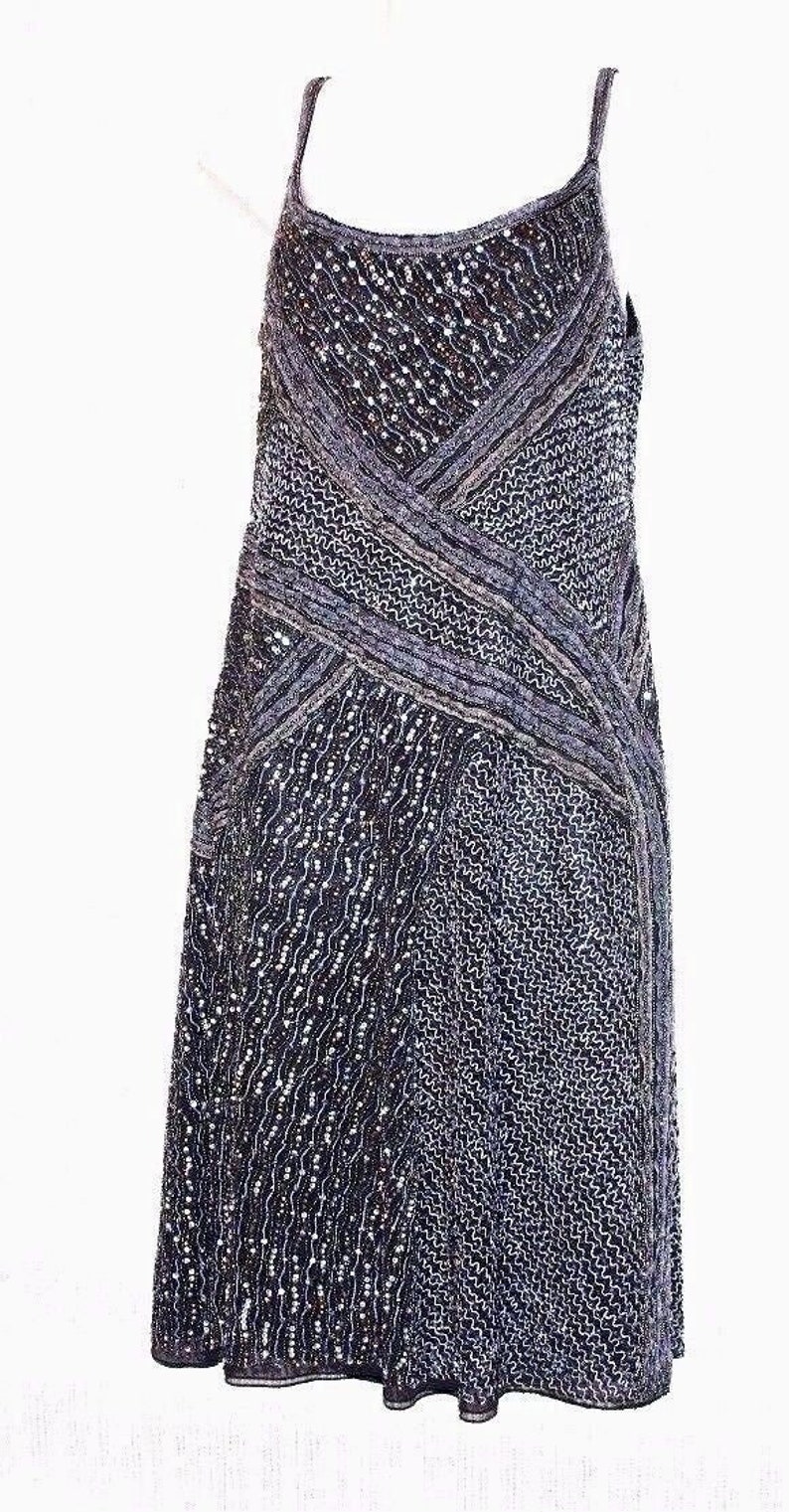 May include: A dark blue and silver sleeveless dress, reaching to the knee. The bodice has a crisscross design, and the skirt is textured and patterned. The dress has thin straps.