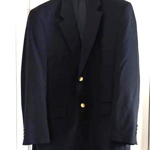 Peut inclure: Un blazer bleu marine avec des boutons dorés. Le blazer est suspendu à un cintre blanc. Il possède deux poches avant et des boutons aux manches. Un style classique.