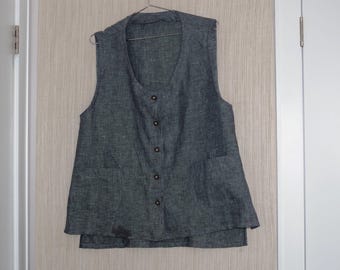 May include: A dark gray vest with a V-neck and button closure. The vest has two front pockets and is hanging on a metal hanger. The garment is made of a textured fabric.