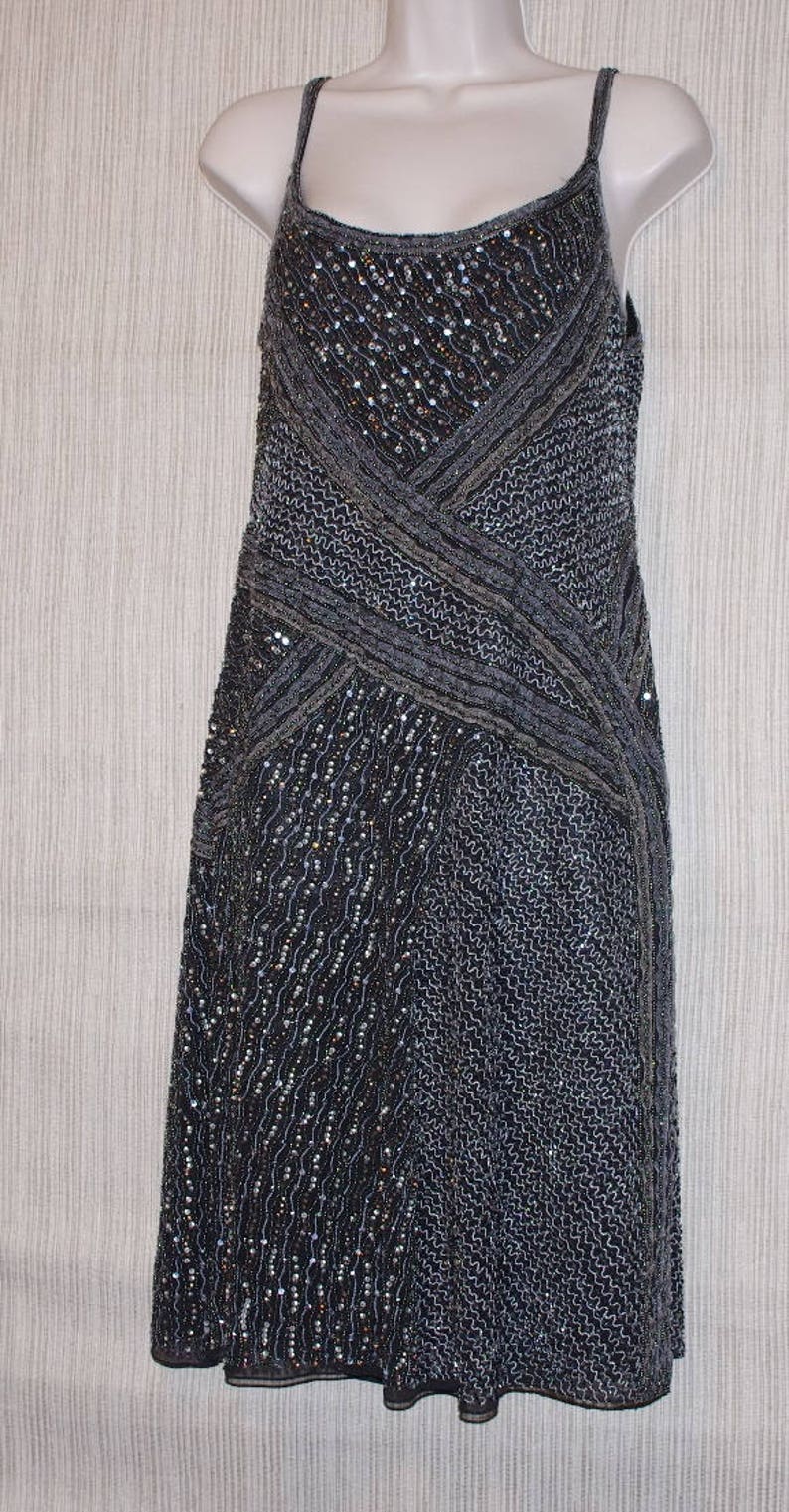 May include: A dark grey, sleeveless dress with a beaded bodice and skirt. The dress features a crisscross design on the bodice and a flowing skirt. The dress is displayed on a white mannequin.