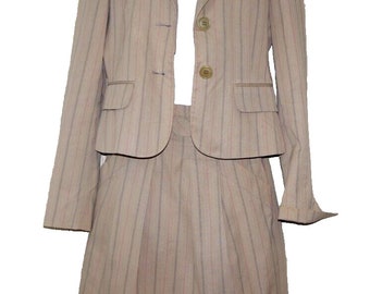 May include: A beige skirt suit with vertical pinstripes. The suit comprises a blazer with two buttons and a skirt. The blazer has two front pockets. The suit is made of a light-coloured fabric with thin, dark stripes.