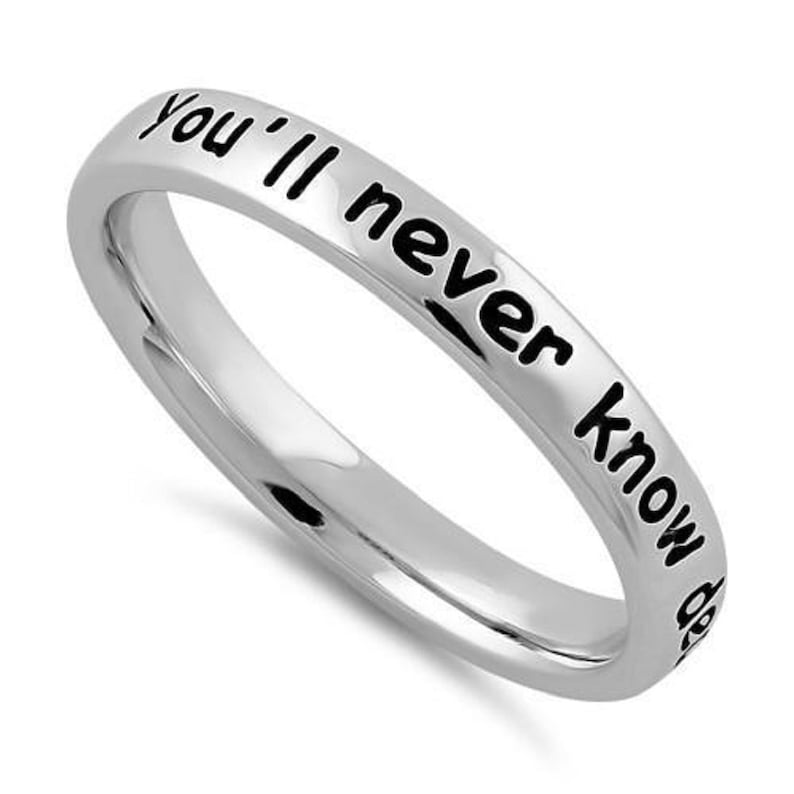 May include: A silver ring with the inscription "You'll never know" in black lettering.