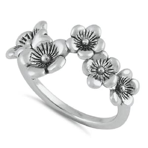 May include: A silver-toned ring featuring a band adorned with a series of four dimensional flower motifs. Each flower has five rounded petals with detailed, radiating lines etched into the surface, centered around a small, raised circular point.