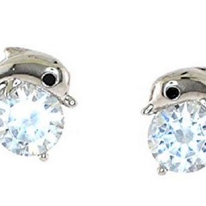 May include: A pair of silver-toned dolphin stud earrings. Each dolphin holds a large, round, clear gemstone. The dolphins have black eyes and are set against a white background. The earrings are a jewelry item.